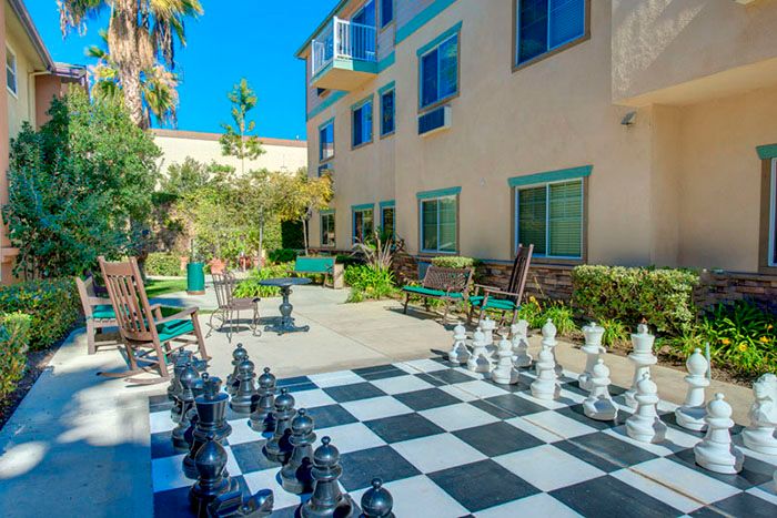 A large outdoor chess set in a sunny garden with a building in the background.