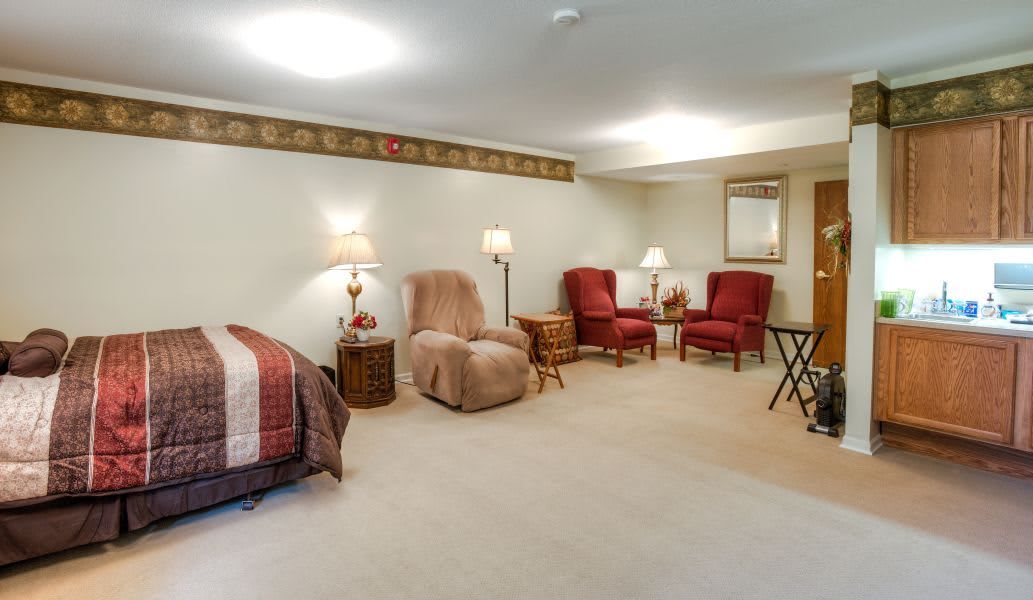A cozy basement living area featuring recliner and red armchairs, a bed, and soft lighting from table lamps.