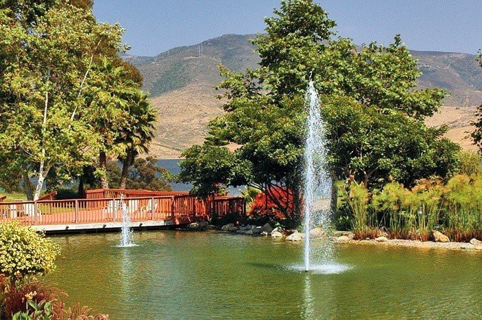 A serene pond with fountains and a red bridge set against a backdrop of mountains.