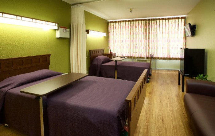 A hospital room with two beds, green walls, and curtains.