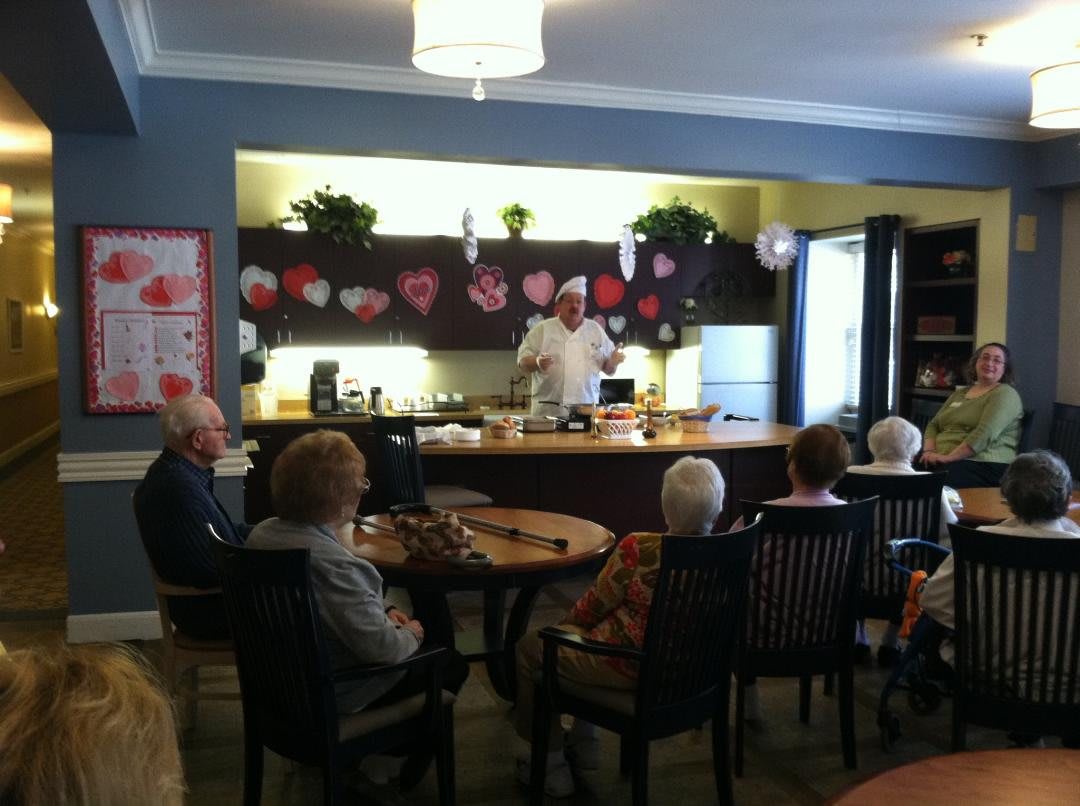 A group of elderly people attending a presentation in a community kitchen.
