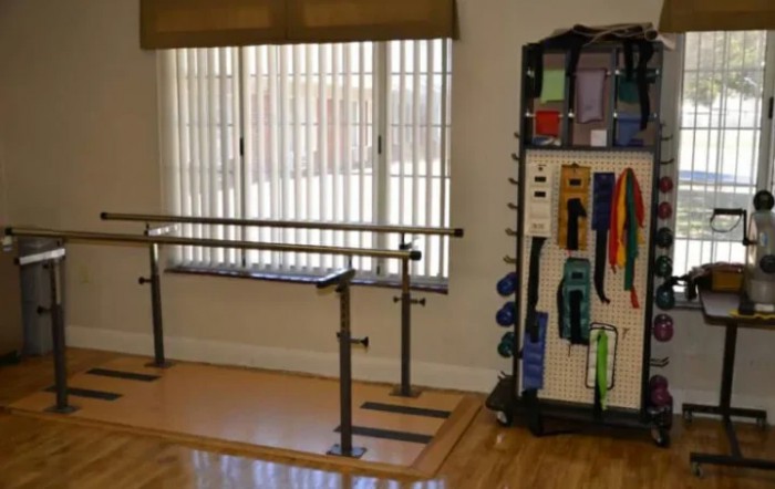A physical therapy room with parallel bars and various exercise equipment.