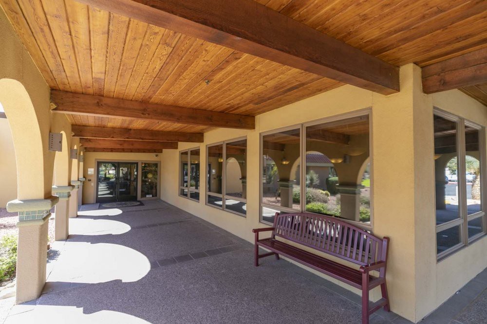 A covered outdoor corridor with a wooden bench and large windows.