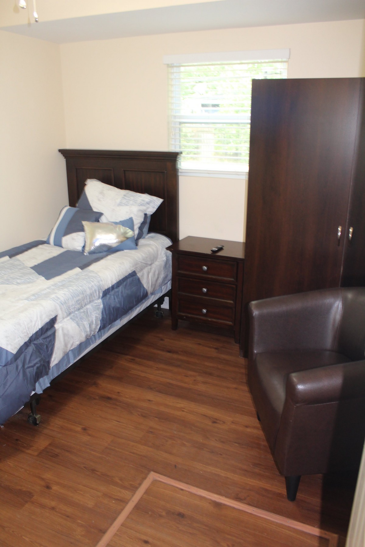 A cozy bedroom with a single bed, wooden furniture, and a comfortable chair.