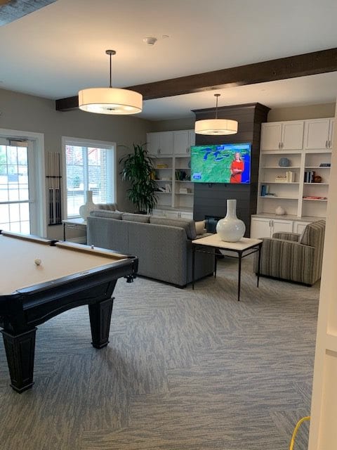 A modern living room with a pool table, cozy seating area, and a television mounted on a wall with built-in shelves.