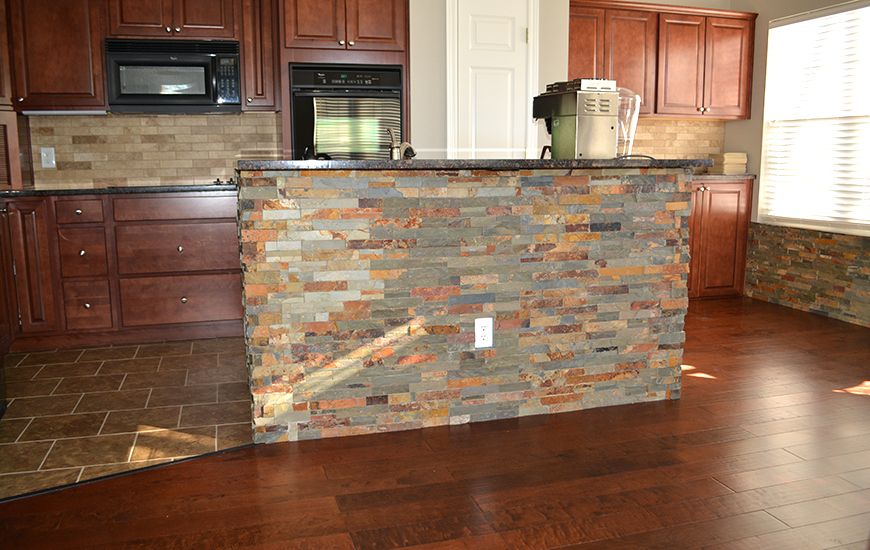 A kitchen with a stone veneer counter and hardwood flooring.