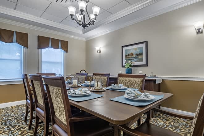 A neatly arranged dining room with a wooden table set for four, featuring a chandelier and elegant decor.