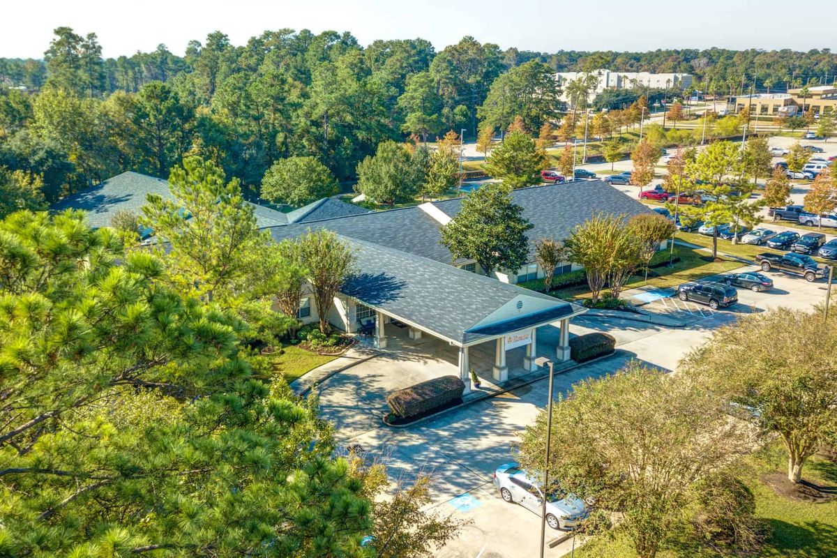 Aerial view of a building surrounded by trees and a parking lot in a suburban area.
