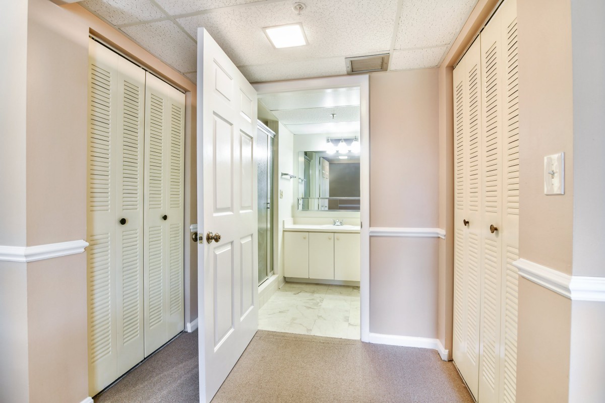 A hallway with wooden doors leading to a mirrored bathroom.