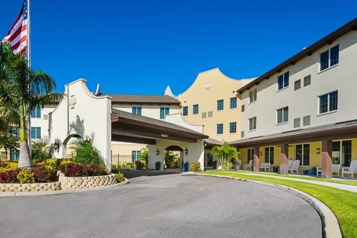 A modern hotel building with a covered entrance and landscaped surroundings on a bright sunny day.