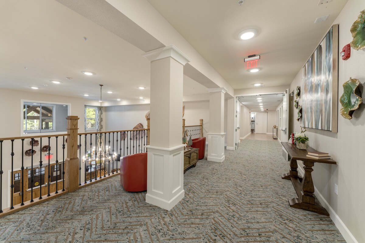 A well-lit interior hallway with carpet flooring and columns, featuring comfortable seating and decorative elements.