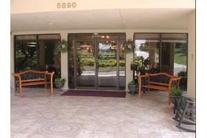 A building entrance with glass doors, flanked by benches and potted plants.