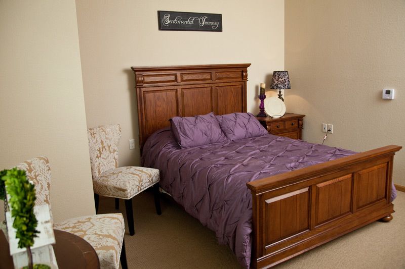 A cozy bedroom featuring a wooden bed with purple bedding, an upholstered chair, and a lamp.