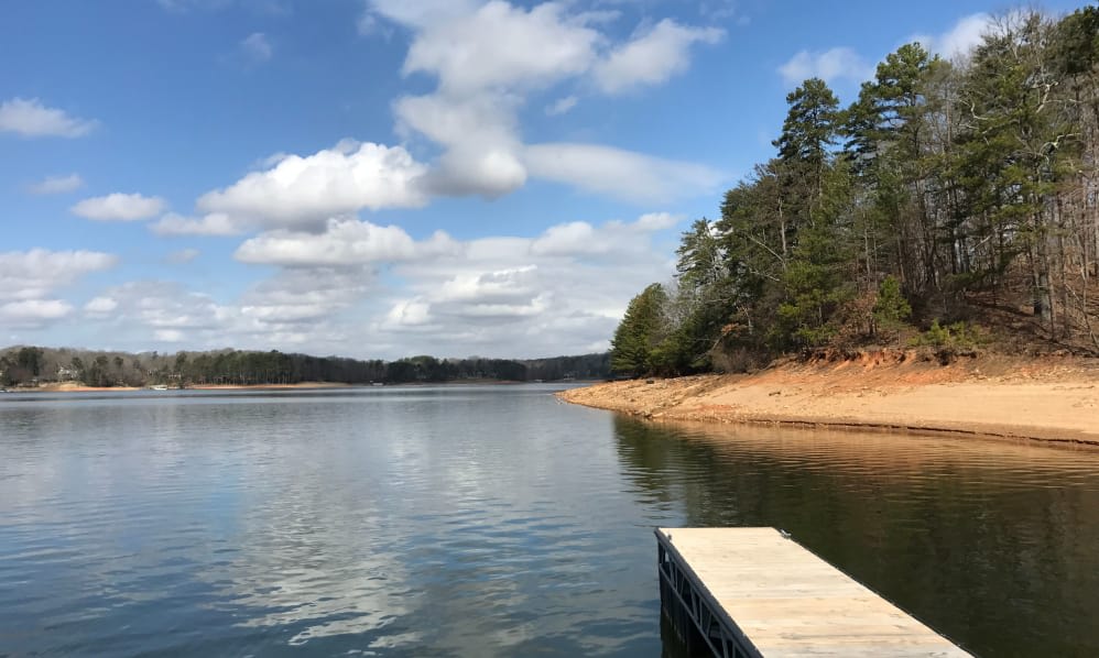 A peaceful lake view with a dock extending into the water, surrounded by trees and under a partly cloudy sky.