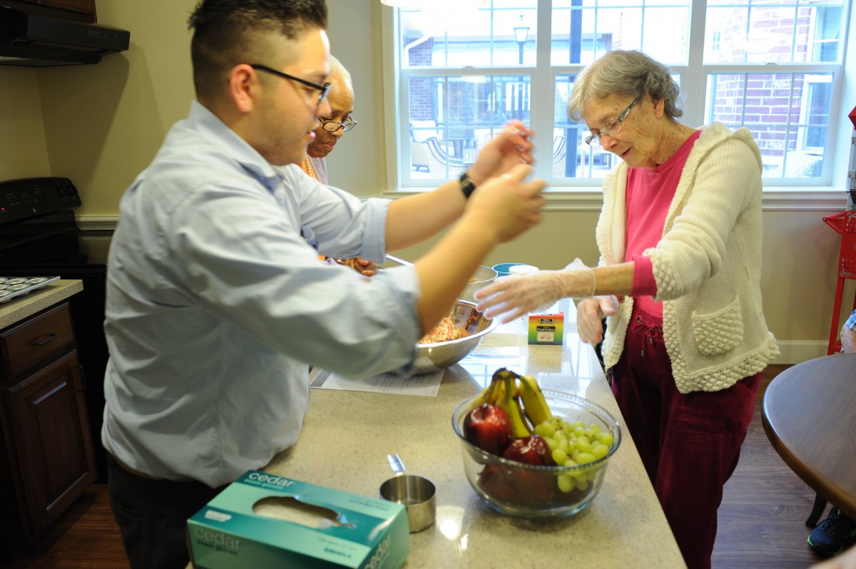 Three people preparing food together in a kitchen with a bowl of fruit on the counter.