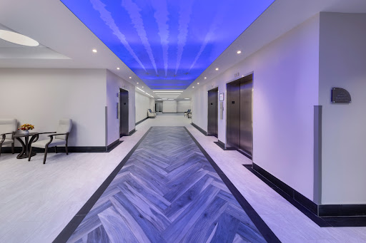 A modern hallway featuring elevators, stylish tile flooring, and a captivating blue ceiling.