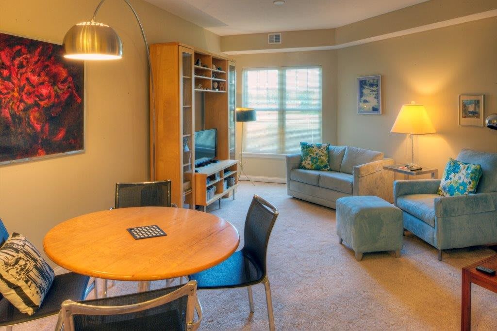 A cozy living room with a dining area featuring a round table, chairs, a comfortable sofa set, and a television stand near a large window.