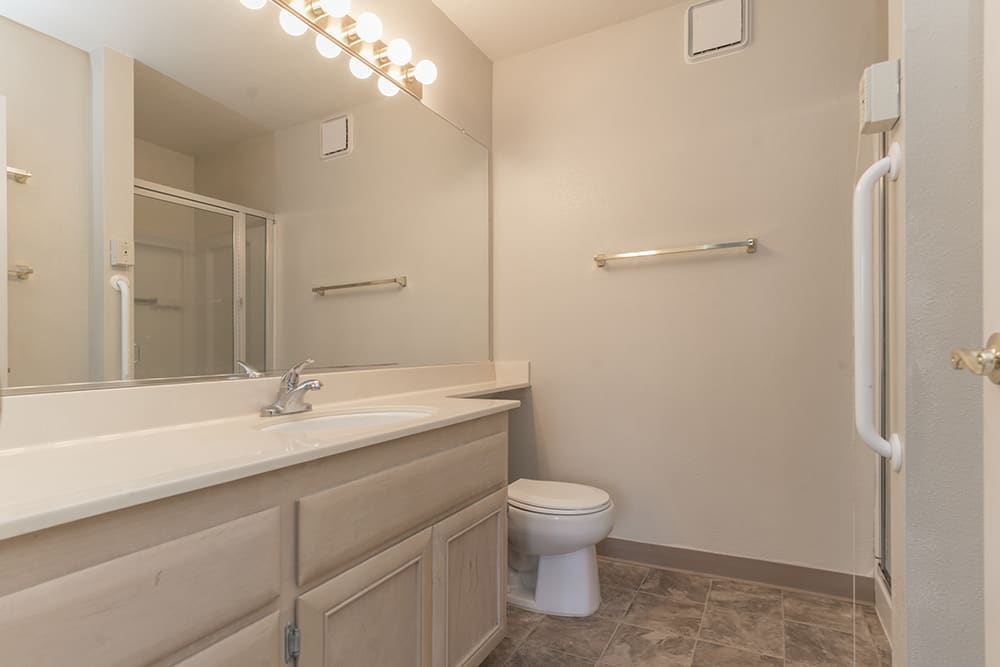 A clean and modern bathroom with a large mirror, vanity, and toilet.