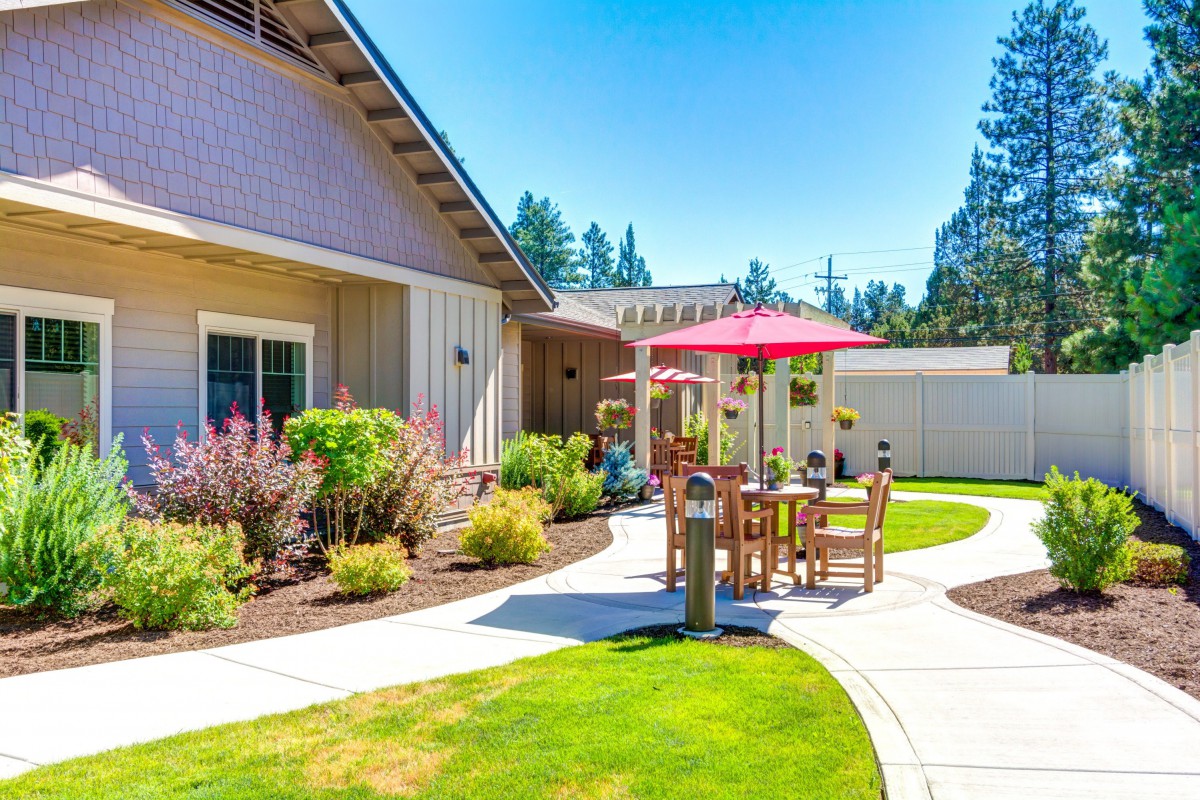 A sunny patio area with outdoor furniture and an umbrella, surrounded by a well-maintained garden and landscaping.