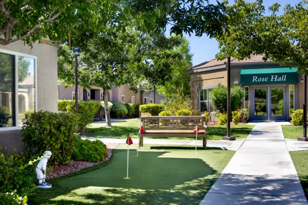 A peaceful garden setting with a bench and putting green surrounded by trees.