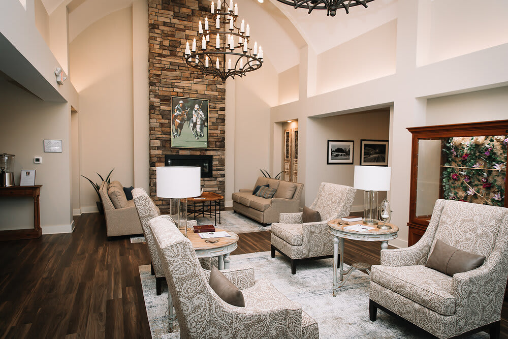 A modern living room with high ceilings, featuring a central fireplace, elegant chandelier, and neutral-toned furnishings.