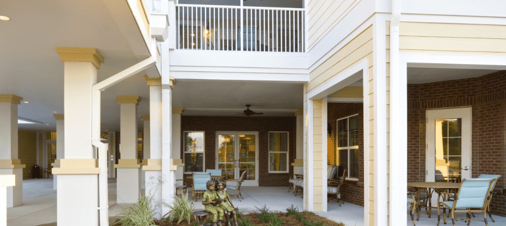 A cozy patio area with outdoor seating and a charming garden sculpture, nestled under an apartment balcony.