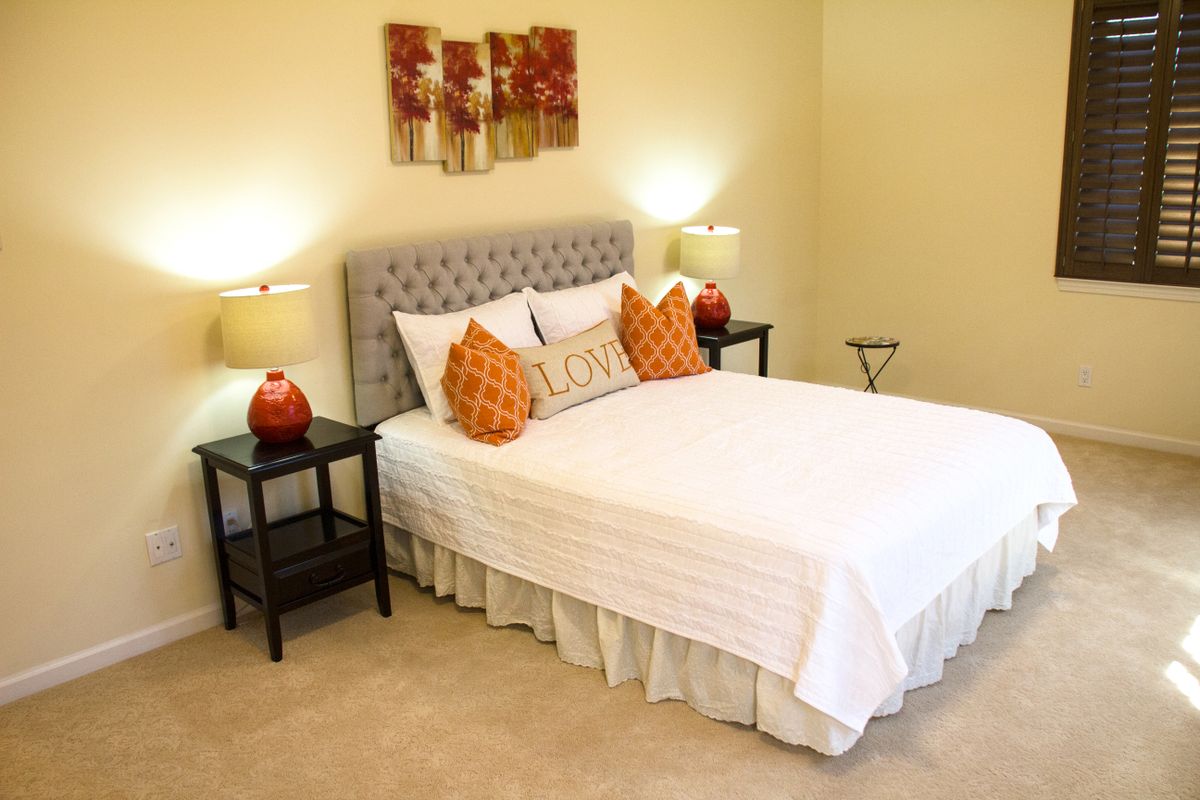 A well-decorated bedroom with a neatly made bed, side tables with lamps, and artwork on the wall.