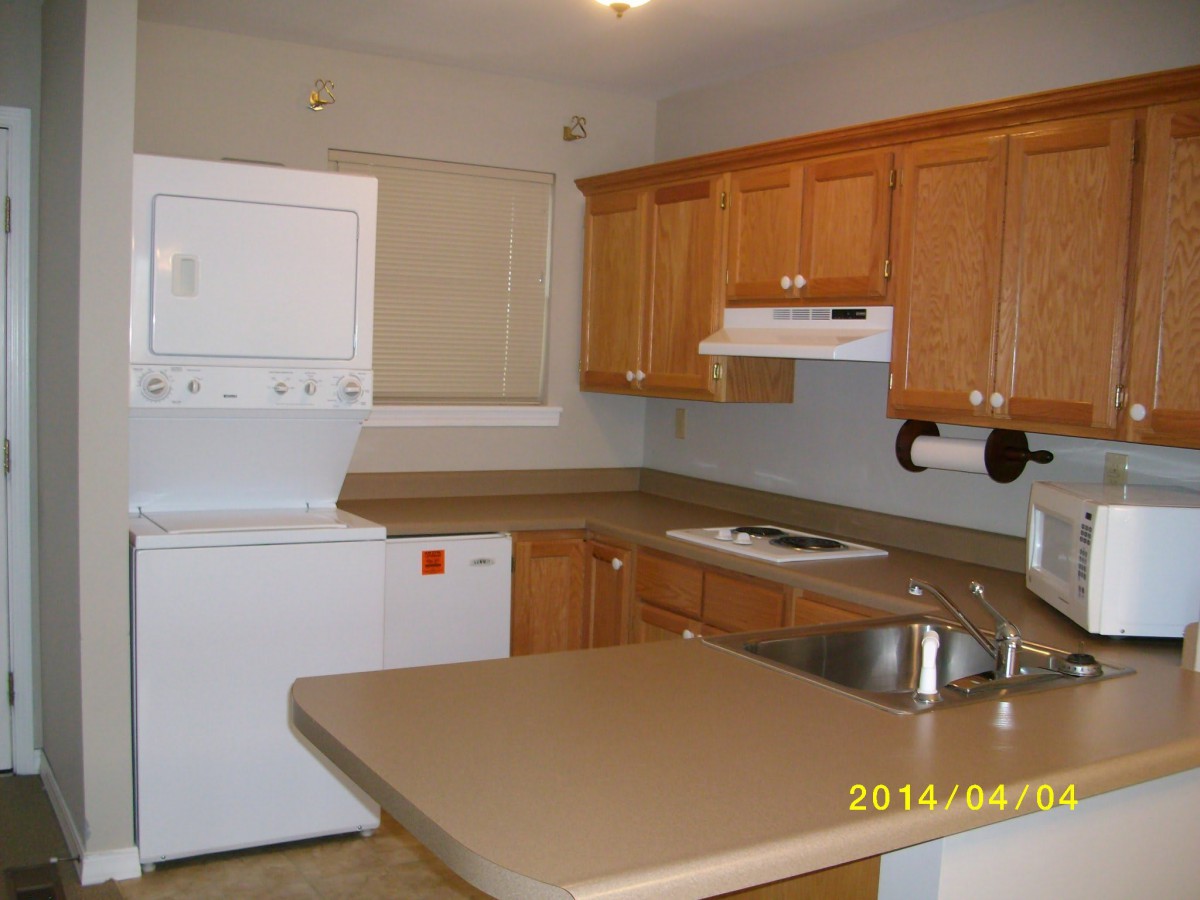A kitchen with wooden cabinets, stacked washer and dryer, and a countertop with a sink.