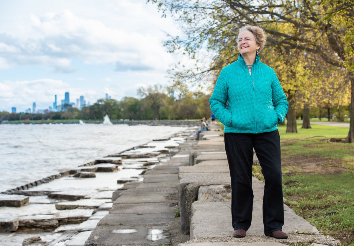 A woman walks along a park path by the waterfront on a crisp autumn day.