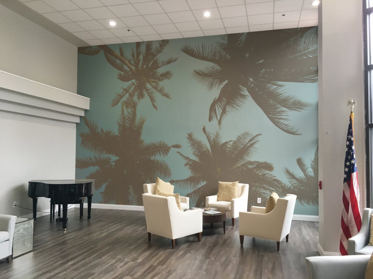 A modern lobby featuring a palm tree wall mural and a cozy seating area with chairs and a coffee table.