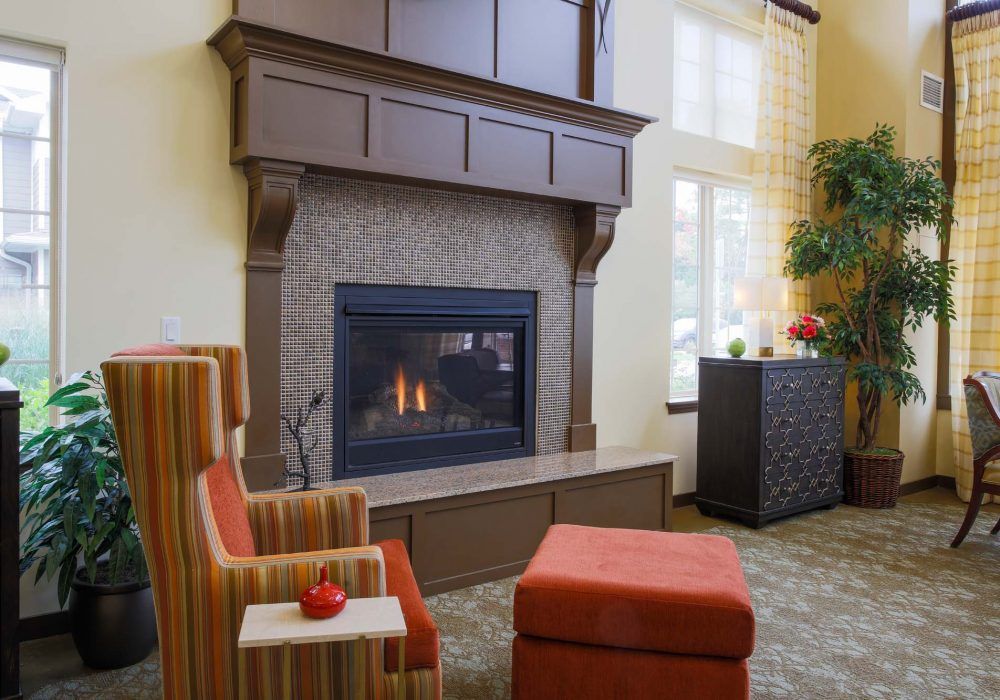 A cozy living room with a warm fireplace, comfortable armchair, and a matching ottoman.