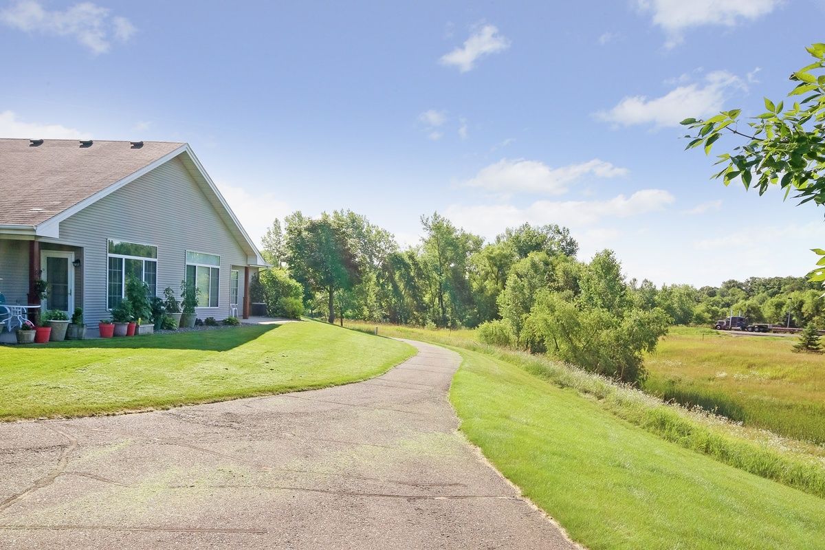 A house with a long driveway surrounded by green lawn and trees under a clear blue sky.