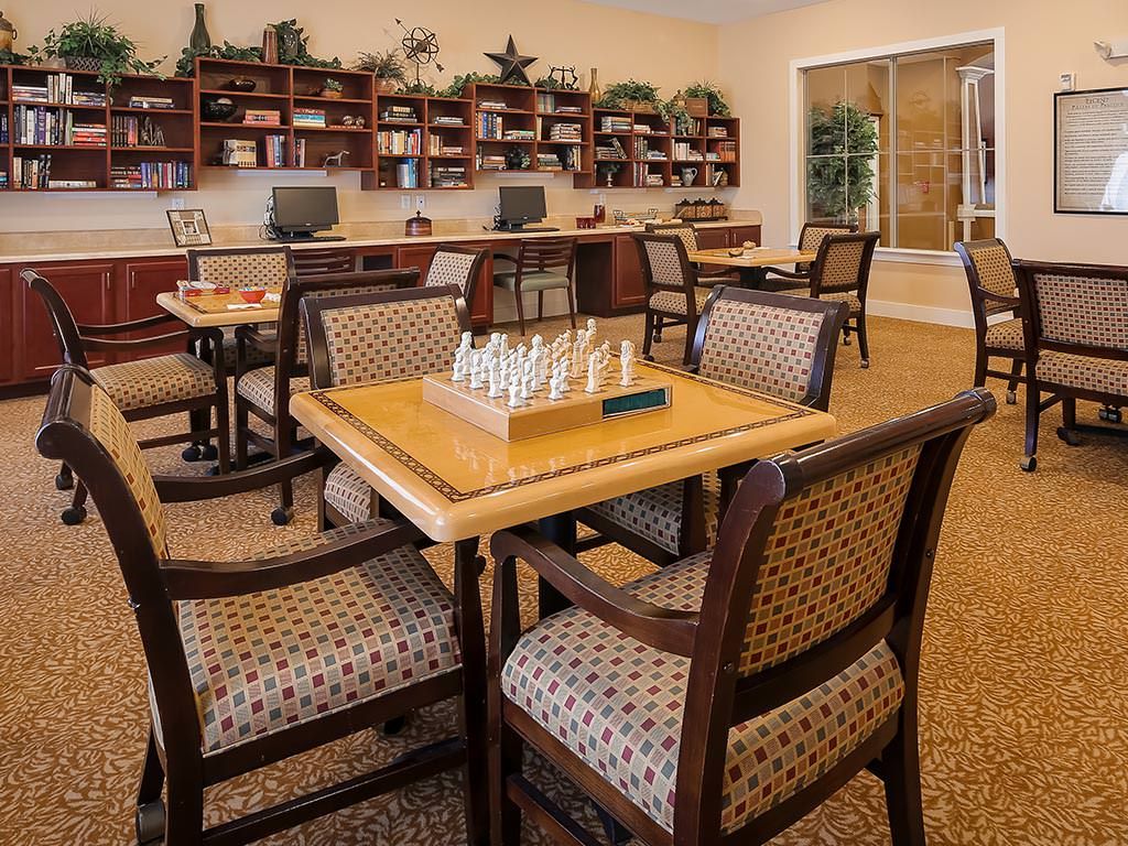 A cozy library with seating areas, bookshelves, and a chess set on the table.
