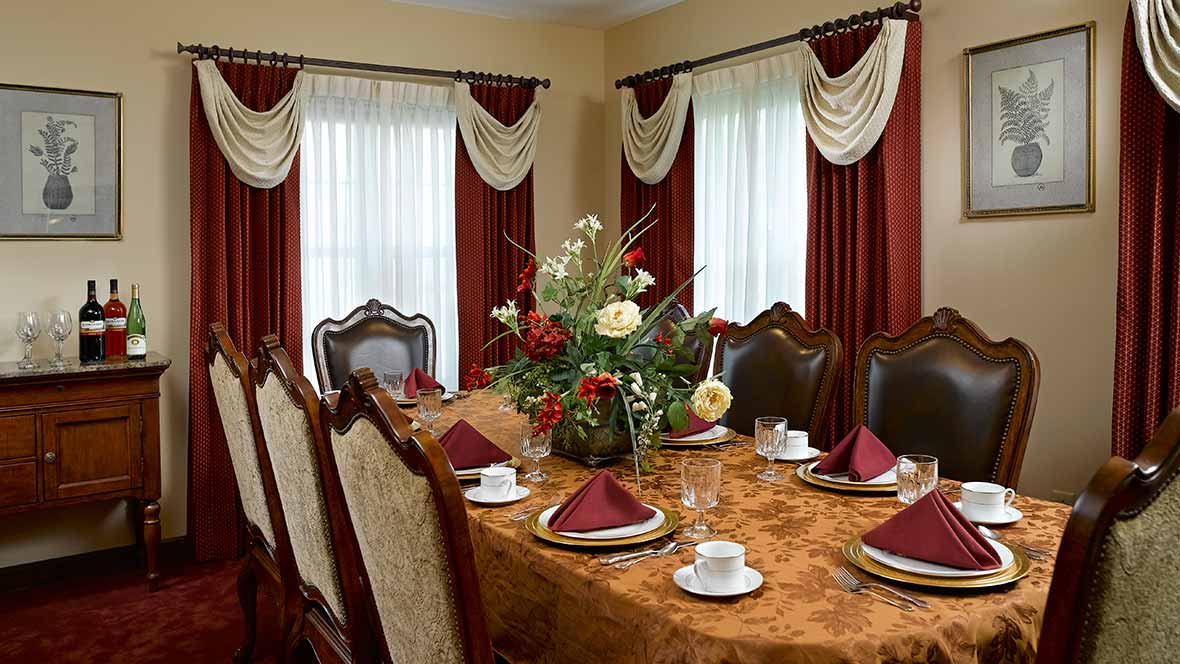 A formal dining room with an elegantly set table, complete with floral centerpiece and rich drapery.