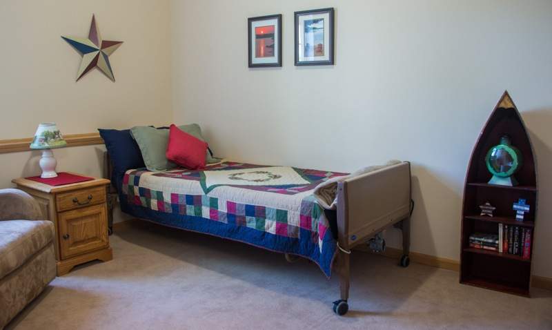 A neatly made bed with a colorful quilt and pillows, in a room with framed pictures on the wall.