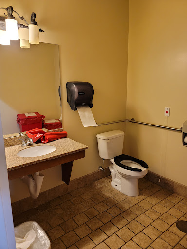 A view of a simple bathroom featuring a toilet, sink, mirror, and hand dryer with red towels.