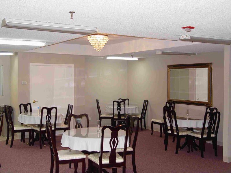 An empty dining room with round tables covered in white tablecloths and wooden chairs, illuminated by a chandelier.