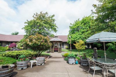 A peaceful garden area with a pathway leading to a gazebo, surrounded by lush greenery and outdoor seating.