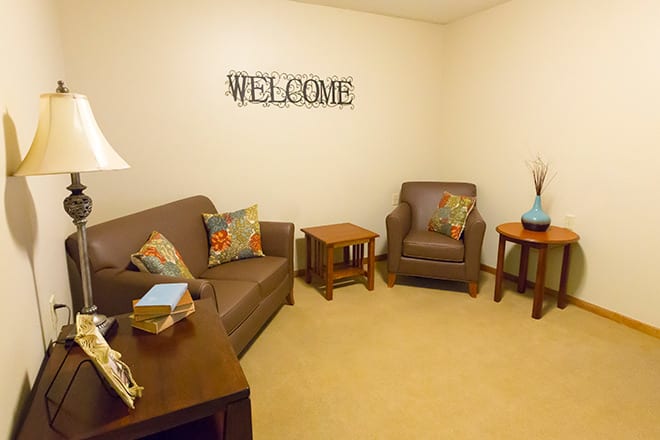 A cozy living room with a sofa and armchair, accented by colorful pillows and a 'WELCOME' sign on the wall.