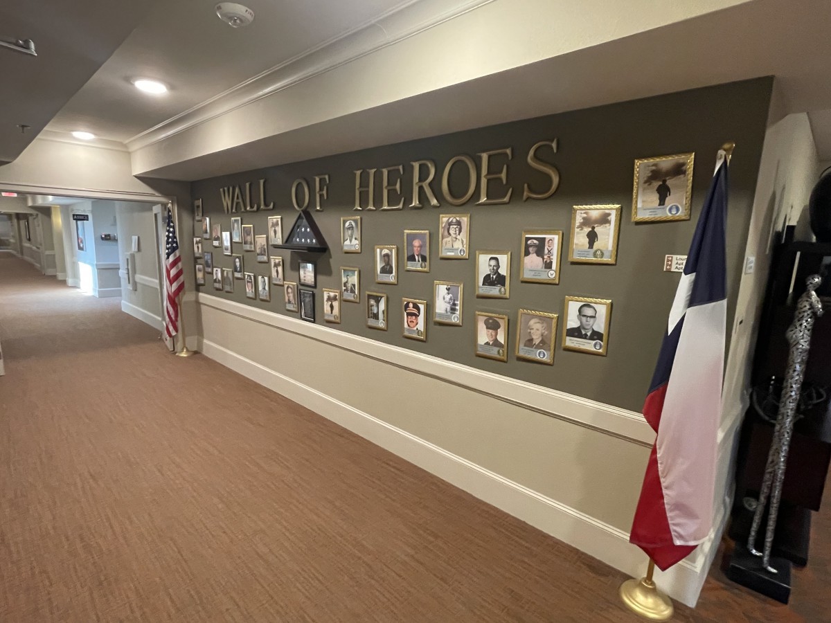 A hallway display titled 'Wall of Heroes' featuring photographs and memorabilia in tribute to military service members, accompanied by American and Texas flags.