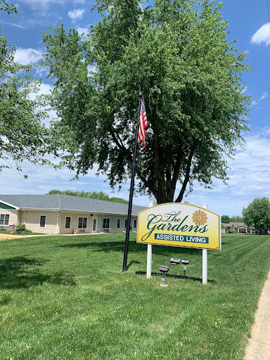 A peaceful community setting featuring a sign for a local establishment, surrounded by greenery and under a clear blue sky.