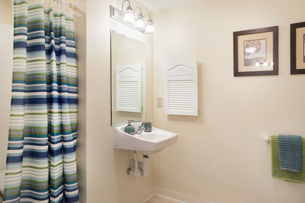 A clean bathroom with a wall-mounted sink, mirror, and colorful shower curtain.