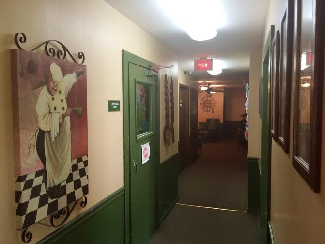A decorated hallway with paintings and a green door under warm lighting.