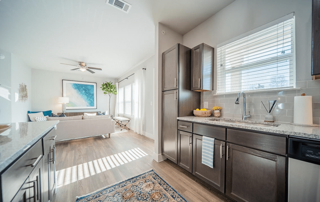 A modern open-concept living area with a kitchen, featuring natural light and wood flooring.