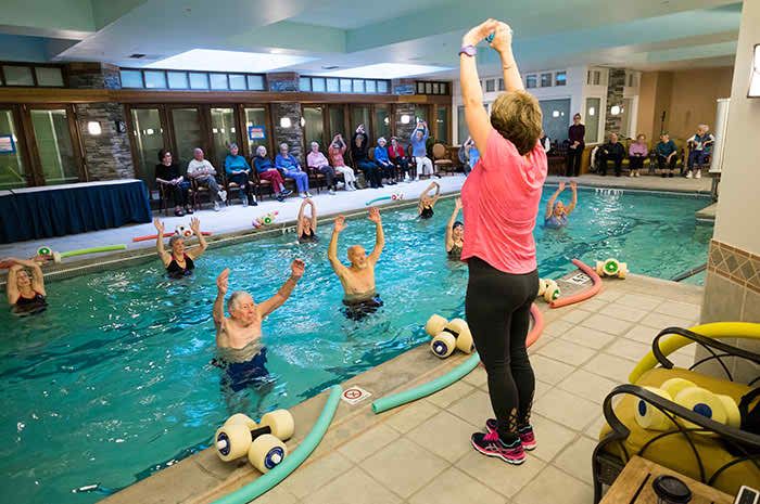 A group of seniors participating in a water exercise class, guided by an instructor on the poolside.