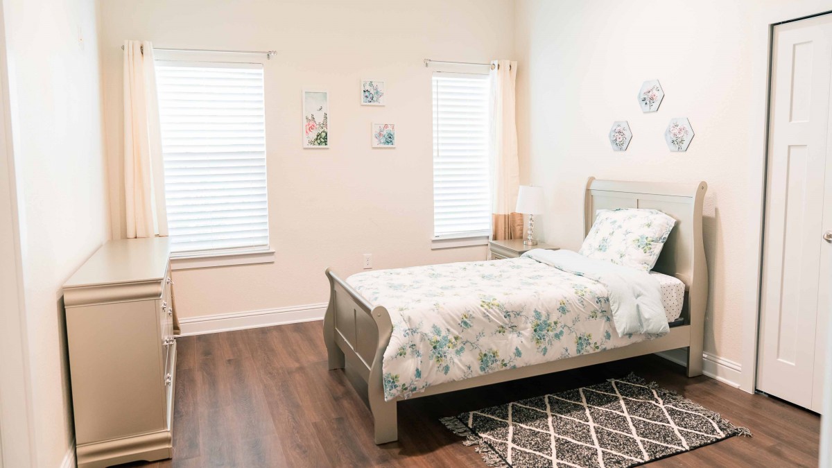 A cozy bedroom with a floral-patterned bedspread, wooden flooring, and minimalistic decor.