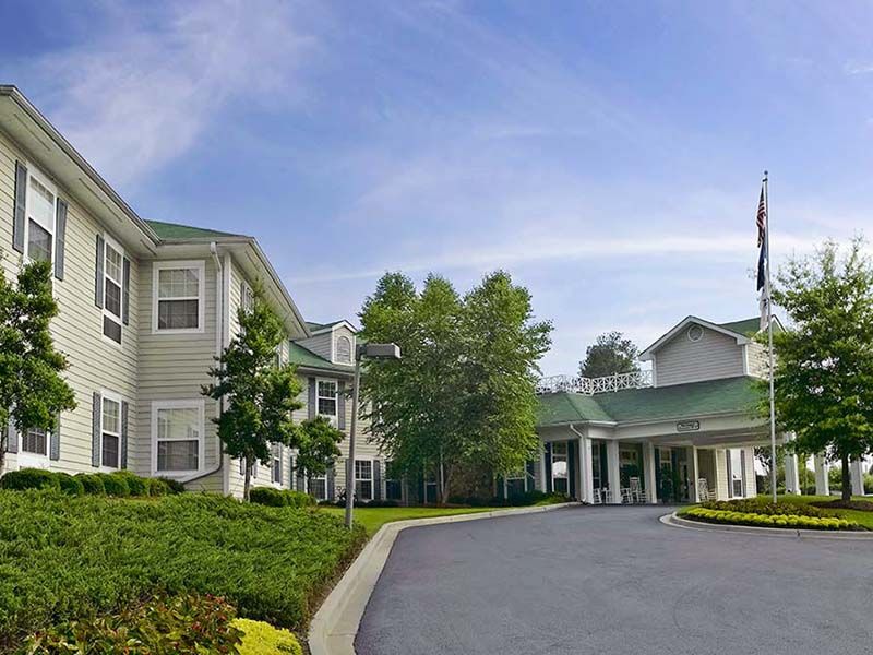 A residential building with a driveway and surrounding trees under a clear blue sky.