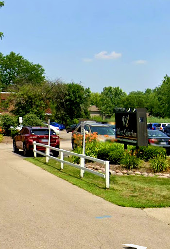 A scenic view of a parking lot with several cars, surrounded by lush greenery and a welcoming sign.