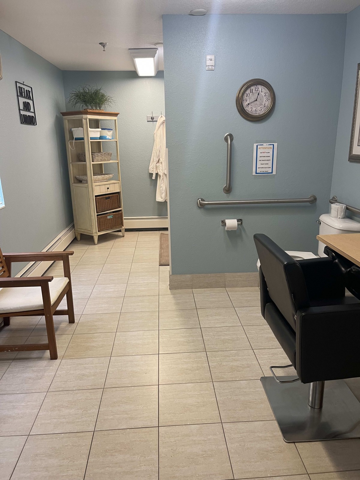 A clean and organized waiting area in a medical office, featuring chairs, shelves, a clock, and tiled flooring.