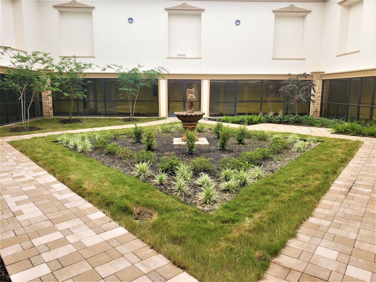 A serene courtyard garden with a central fountain surrounded by greenery and well-maintained landscaping.